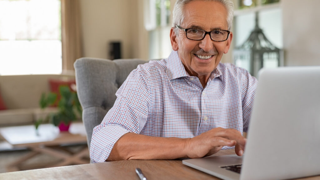 A cheerful senior citizen works with a laptop