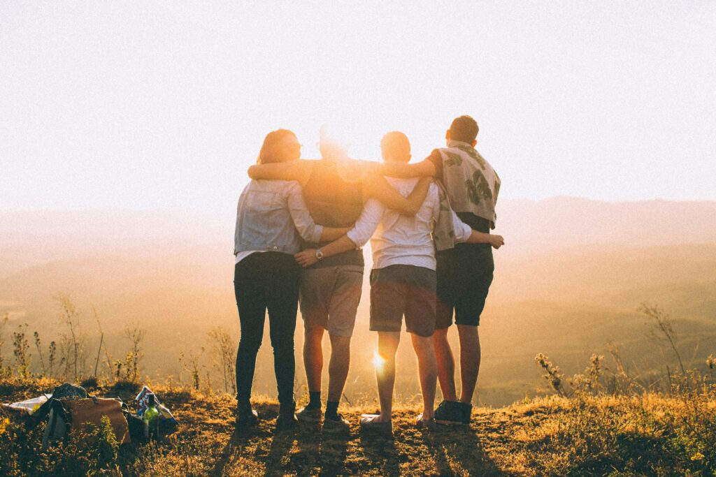 Eine vierköpfige Familie steht mit dem Blick in den Sonnenuntergang. Sie zeigen dem Fotographen den Rücken, sie haben Einander die Arme auf die Schultern gelegt.