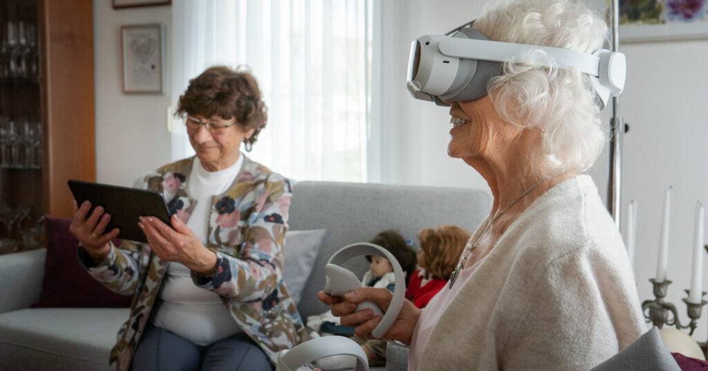 Zwei ältere Damen trainieren gemeinsam mit einer VR-Brille und einem Therapie-Tablet